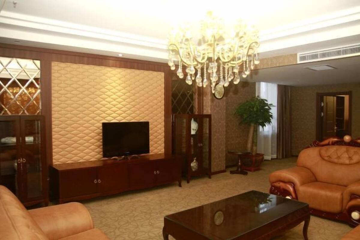 A living room with a television, leather sofa, and a chandelier.