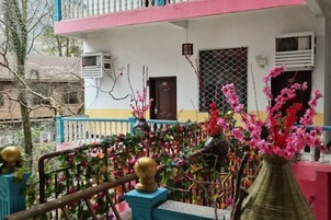 Un balcón con barandilla, un jarrón con flores rosadas y un edificio al fondo.