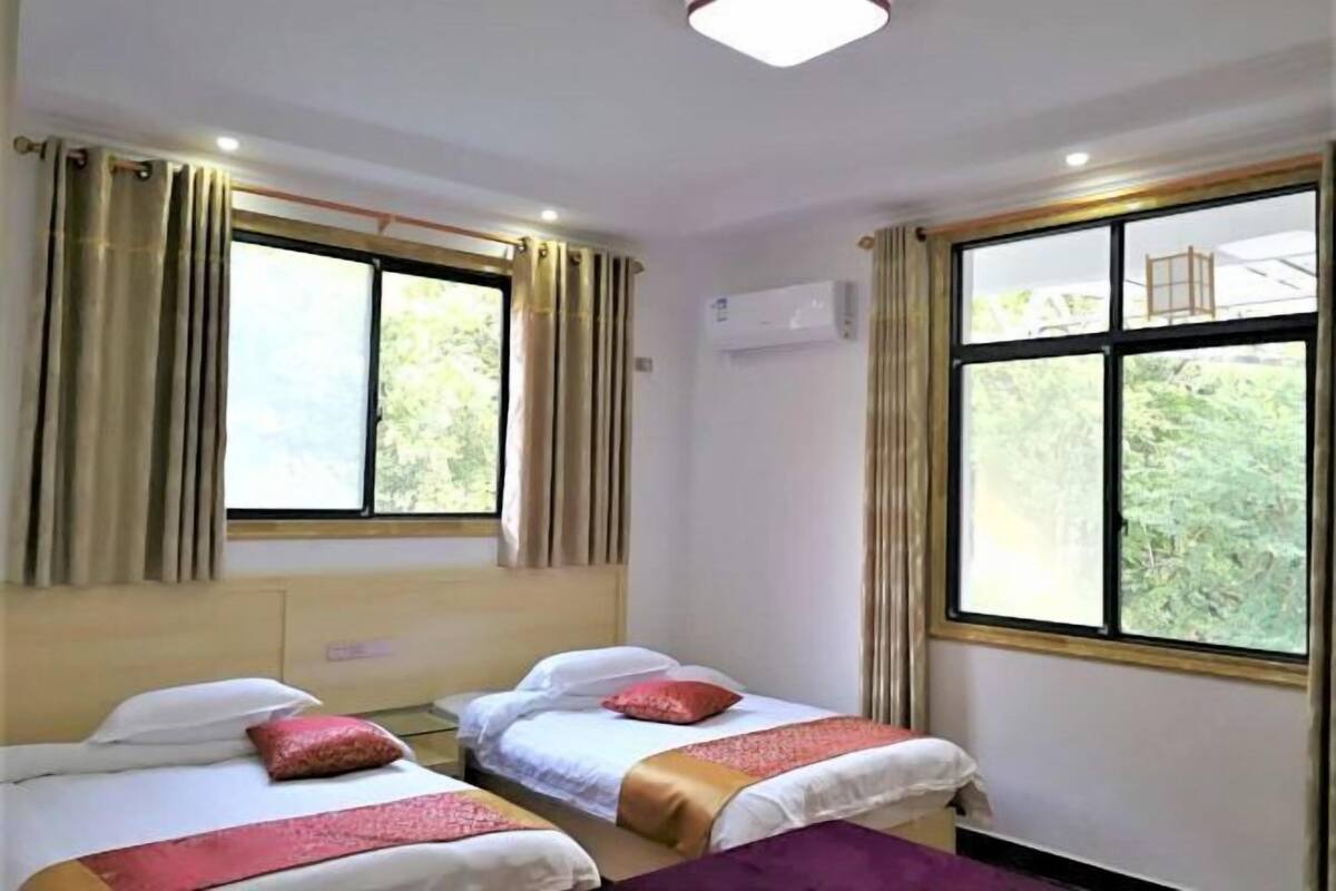Een hotelkamer met twee bedden, een raam met gordijnen, een airconditioning en uitzicht op groen.