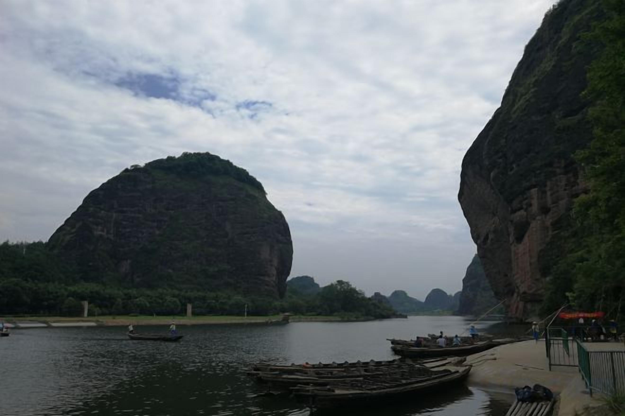 A river with boats, a dock, and a large rock formation.