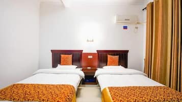 Quarto de hotel com duas camas de solteiro, cabeceira de madeira, uma mesinha e uma janela com cortinas.