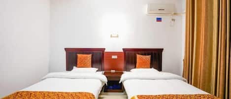 A hotel room with two single beds, a wooden headboard, a small table, and a window with curtains.