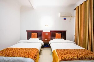 Habitación de hotel con dos camas individuales, cabecero de madera, una mesita y una ventana con cortinas.