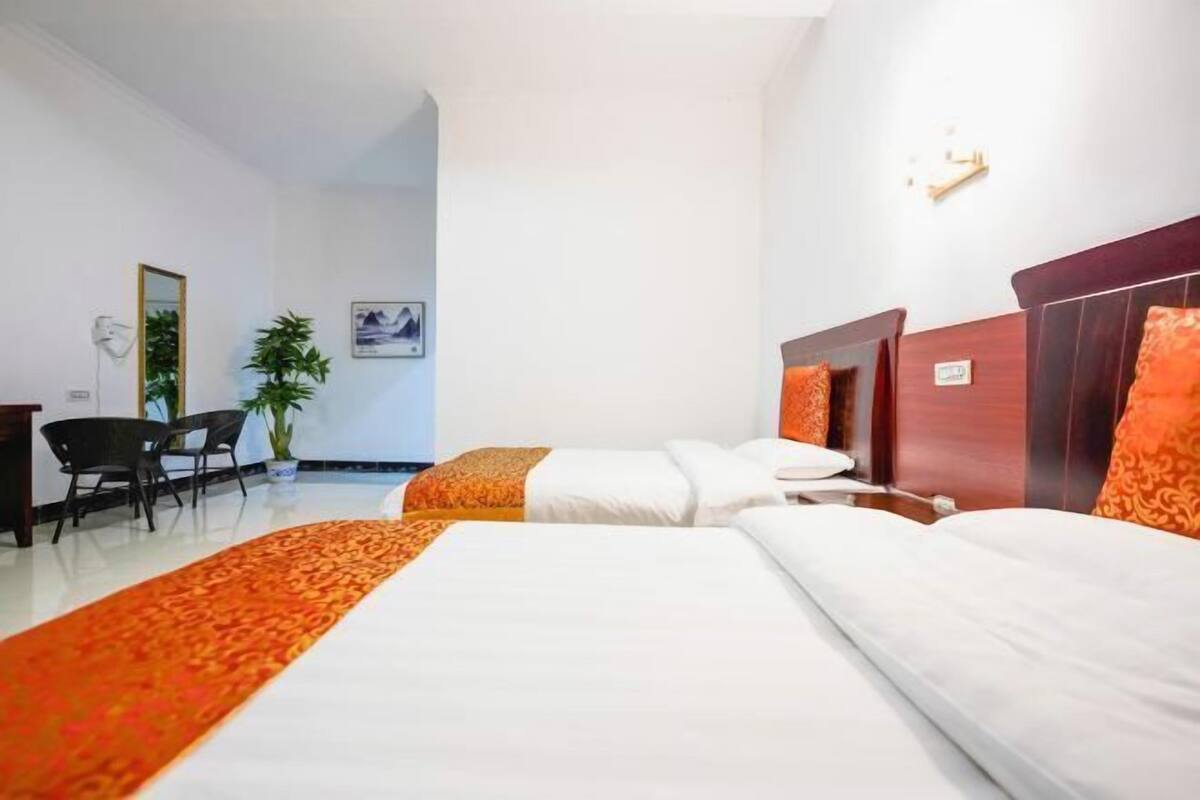 Een hotelkamer met twee bedden, een bureau, stoelen, een potplant en een wandlamp.