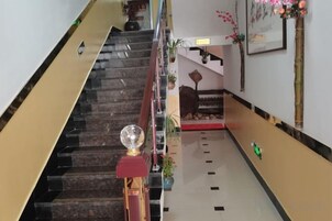 Un escalier d’hôtel avec une rampe rouge, une sphère décorative et un objet vert posé sur le sol.