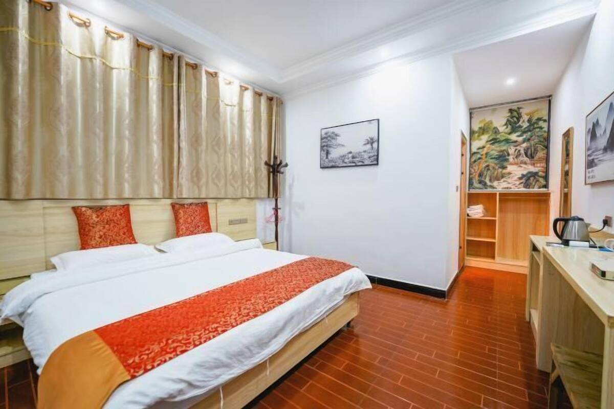 Een hotelkamer met een bed, gordijnen, een schilderij, een bureau en een kledingkast.