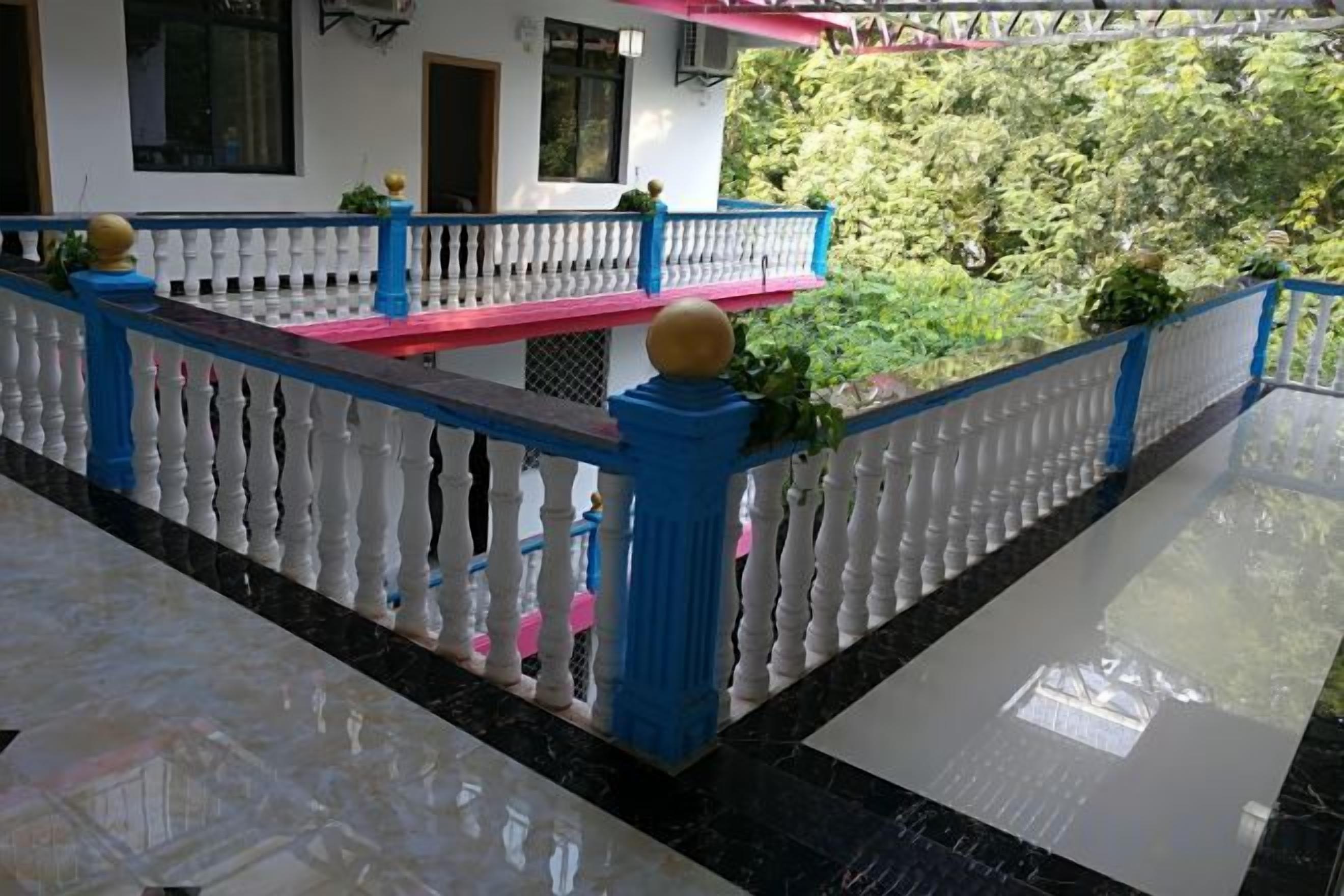 Een balkon met een witte balustrade en blauwe accenten, een marmeren vloer en uitzicht op groen.