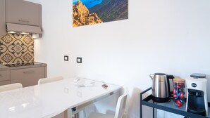 Une cuisine moderne avec une table blanche, une machine à café, une bouilloire et une vue sur un paysage montagneux.