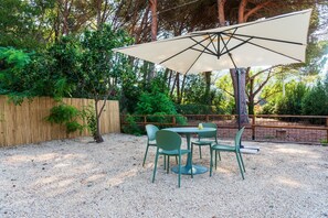 Une terrasse extérieure avec une table et des chaises, entourée d’une clôture en bois et d’arbres.