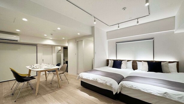 A modern hotel room with a large bed, a dining table with chairs, and a separate seating area. - Modern Studio Apt in Charming Nakamachi Area (Hiroshima)