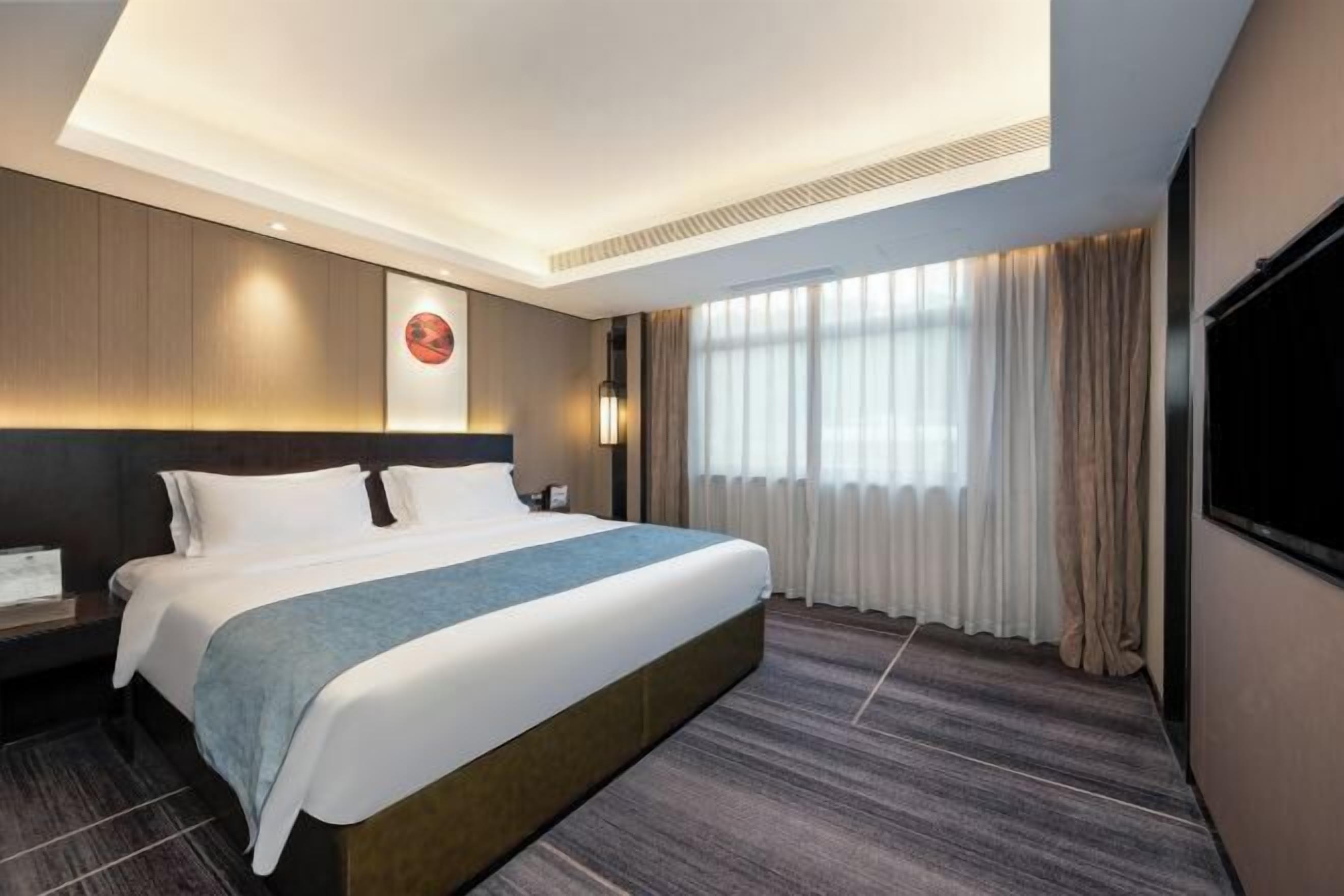 A hotel room with a large bed, a headboard, a flat-screen TV, a nightstand, and a window with curtains.