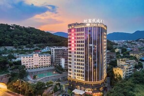A multi-story hotel with a prominent sign at the top, surrounded by other buildings and a hilly landscape in the background. - Yue Hotel (Fuzhou)