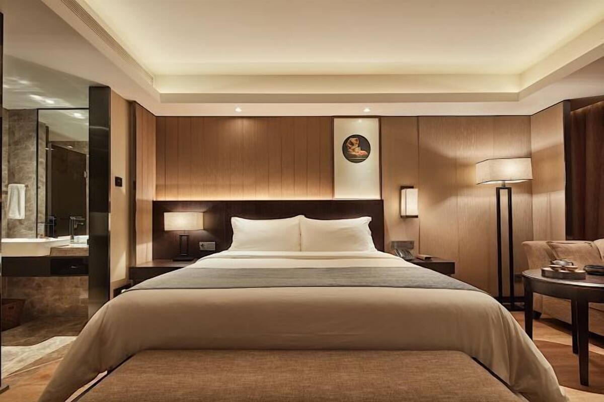 A hotel room with a large bed, a bedside table, a lamp, a wall-mounted artwork, and a mirror.