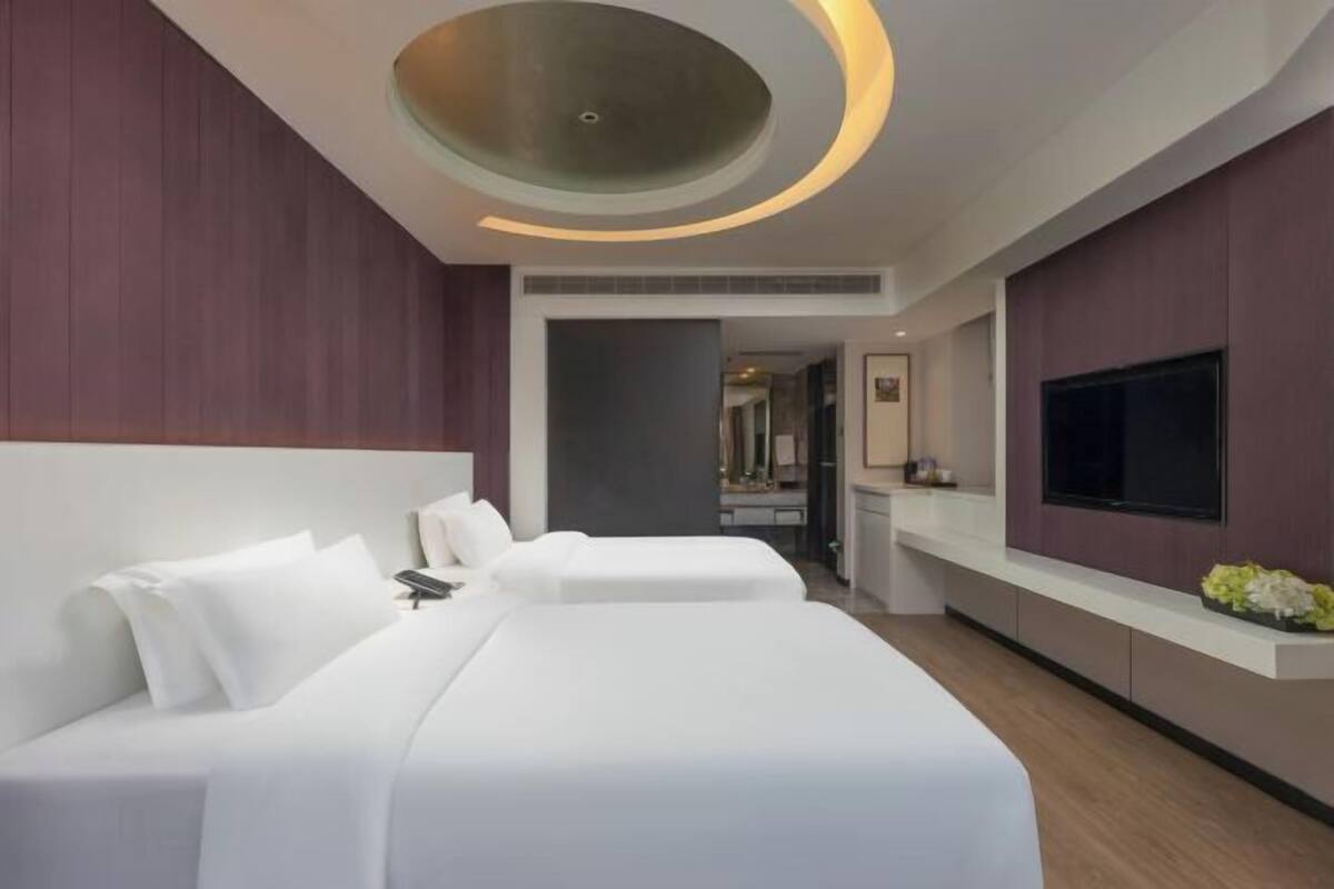A modern hotel room with a large bed, a TV, and a unique ceiling design.
