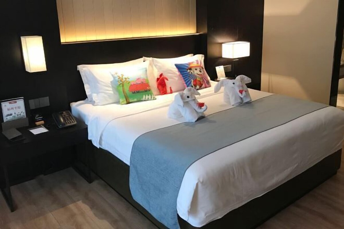 A hotel room with a bed, two bedside lamps, a nightstand with a phone, and decorative pillows.