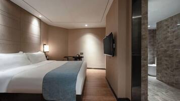 A modern hotel room with a large bed, a flat-screen TV mounted on the wall, a small table, and a nightstand.
