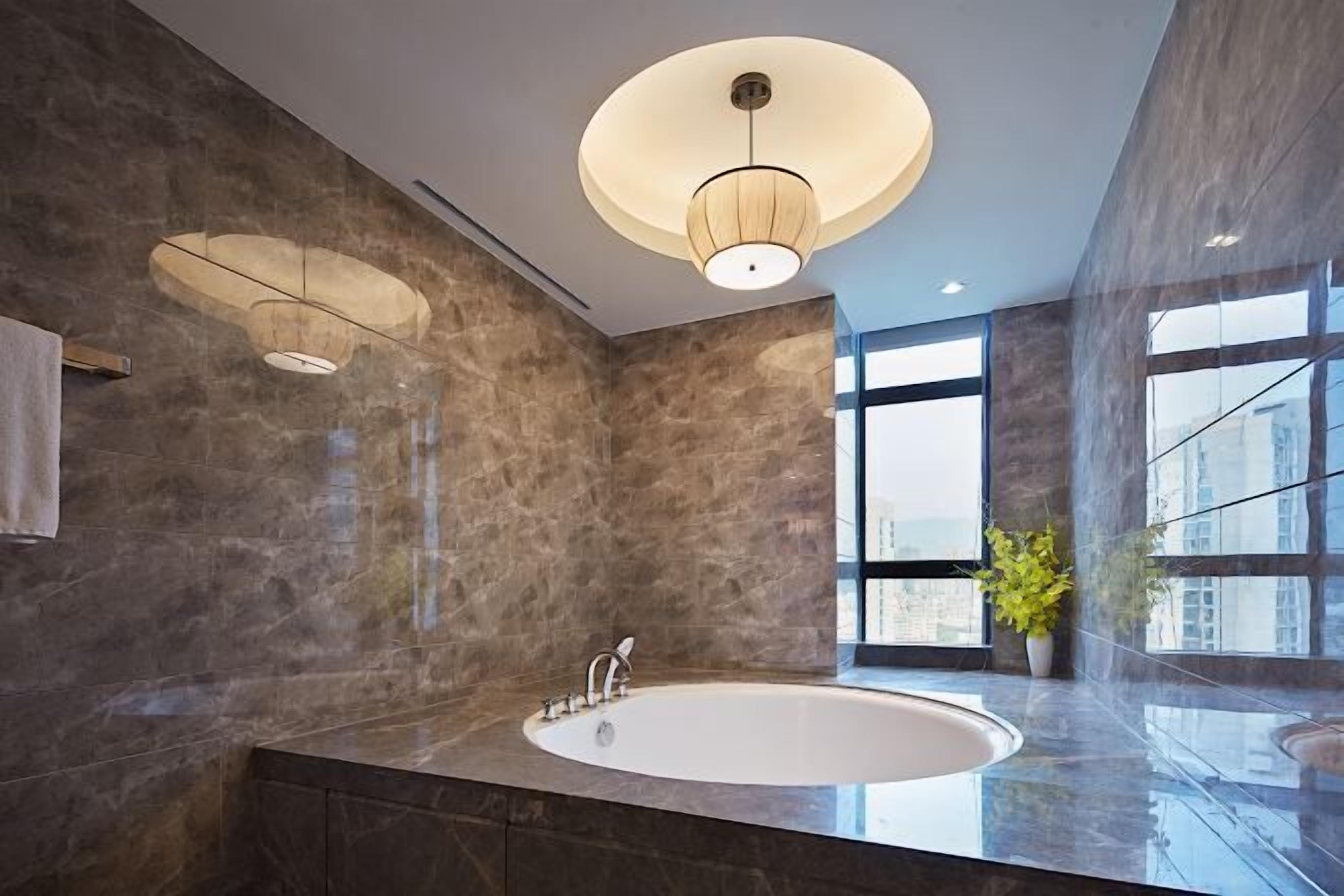 A modern bathroom with a large oval sink, two pendant lights, and a large window providing a view of the city.