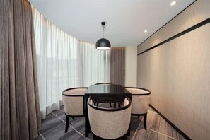 A modern dining area with a round table and four chairs, a pendant light, and a view of a cityscape through large windows with sheer curtains. - Yue Hotel (Fuzhou)