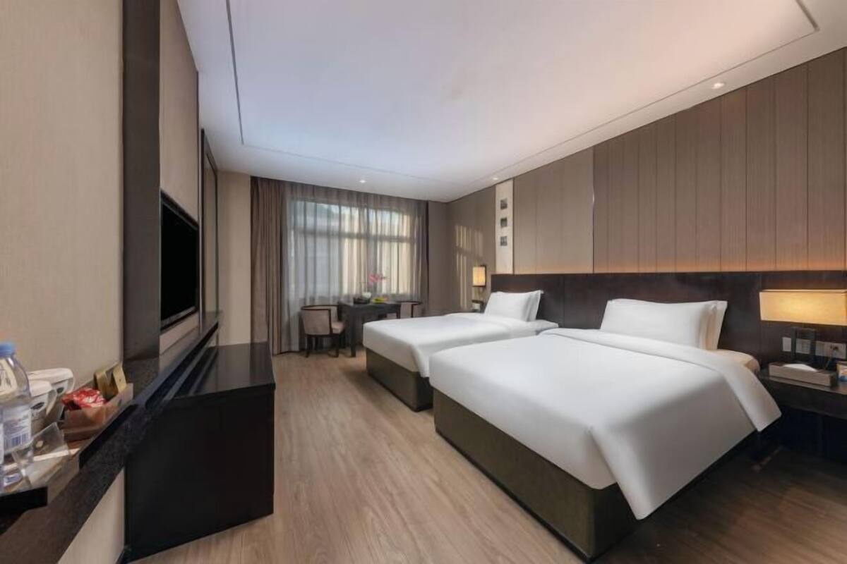 A hotel room with two beds, a desk, a TV, and a minibar.