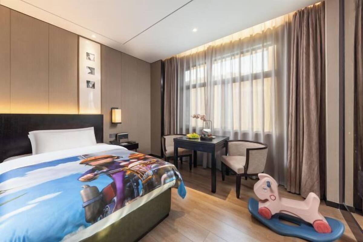 A hotel room with a bed, desk, chair, and a toy horse.