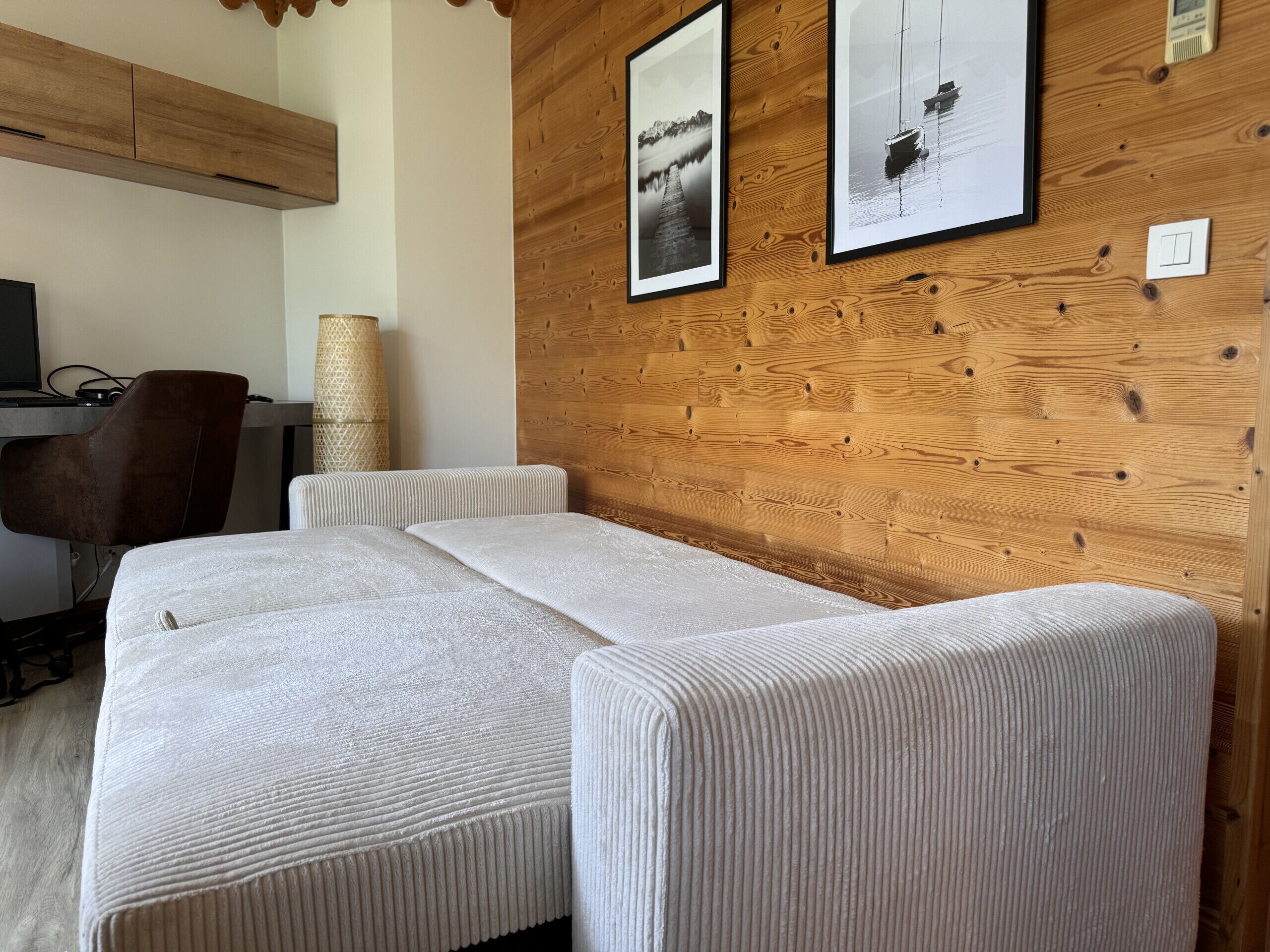Une pièce avec un mur en bois, deux canapés blancs, un bureau avec un ordinateur et des tableaux encadrés.