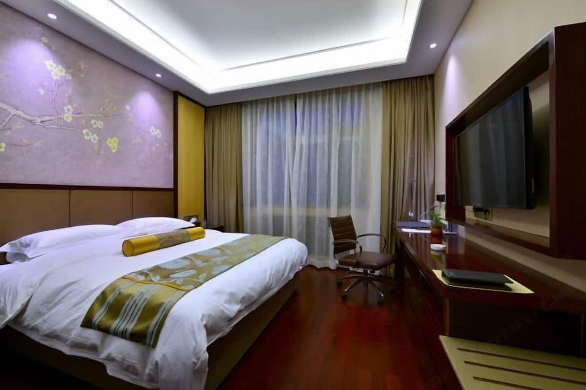 A hotel room with a large bed, a desk with a flat-screen TV, and a large window with curtains.