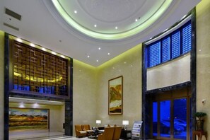 Un hall de hotel con mostrador de recepción, zona de estar y un cuadro grande en la pared.