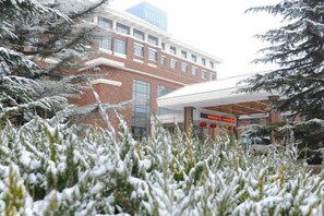 A building with a brick facade, a covered entrance, and snow-covered trees. - Ningwozhuang Hotel (Building 1) (Lanzhou)