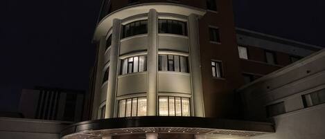 Un hotel de varios pisos con fachada curva, ventanas iluminadas y una entrada visible.