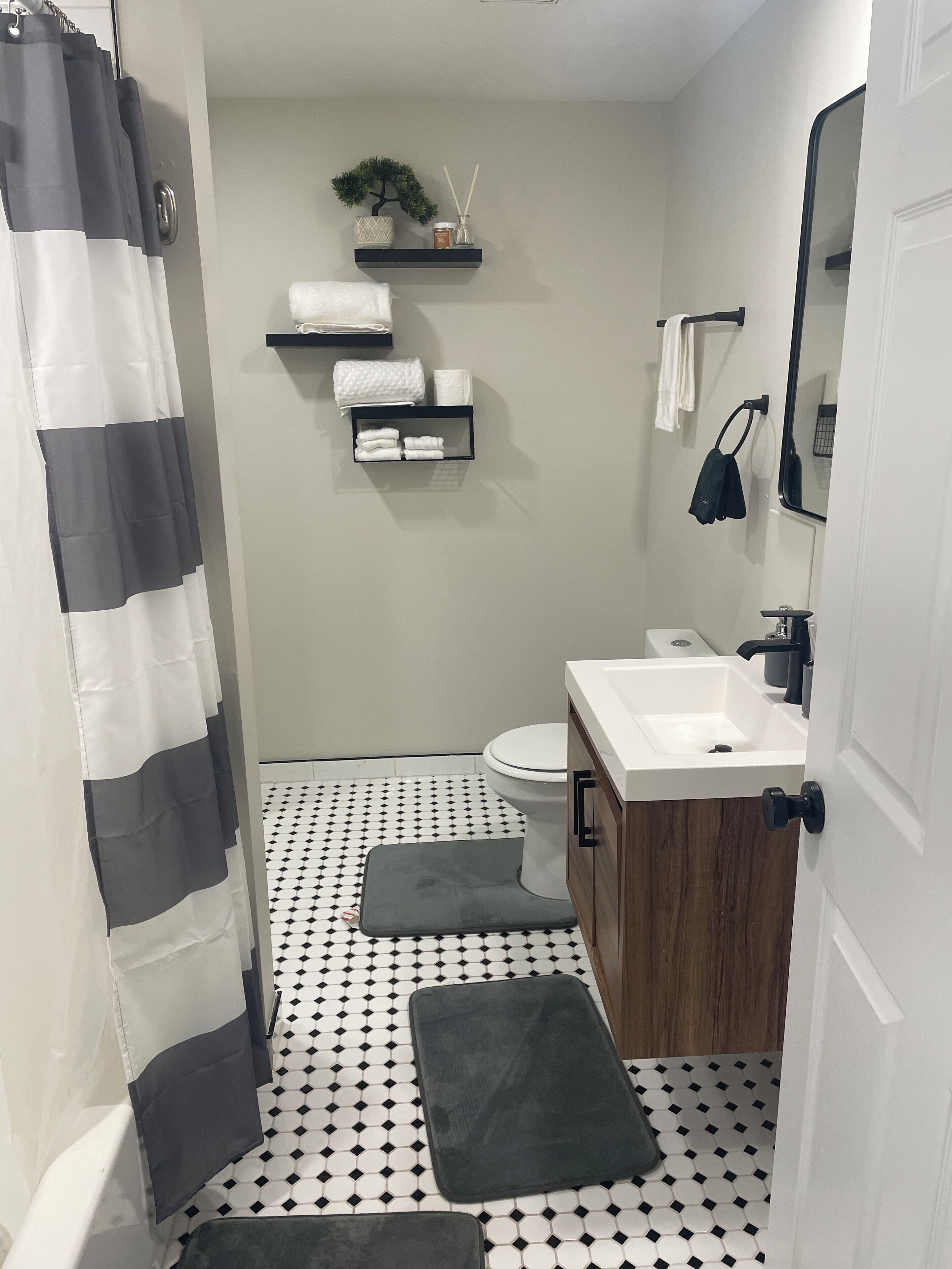 A bathroom with a toilet, sink, and shower curtain. There are towels and a small plant on a shelf.