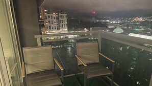 Ein Balkon mit zwei Stühlen und einem Tisch, der auf eine nächtliche Stadtansicht blickt.