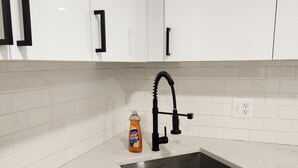 Eine Küche mit weißen Schränken, einer Edelstahl-Spüle und einer Flasche Ajax Spülmittel.