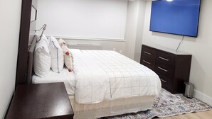 Ein Schlafzimmer mit Bett, Wandfernseher, Nachttisch und kleiner Kommode.