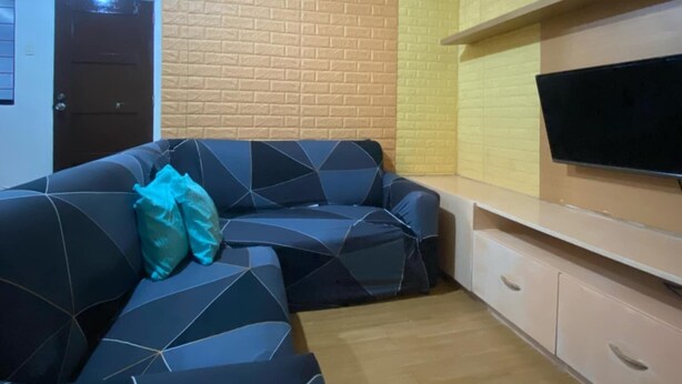 A living room with a sectional sofa, a flat-screen TV mounted on a wooden shelf, and a brick-patterned accent wall. - Deca Homes - Hernan Cortes (Cebu City)