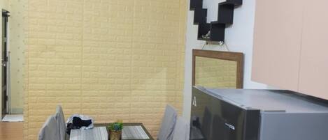 A compact kitchen with a dining table, chairs, a refrigerator, and a wall-mounted shelf.