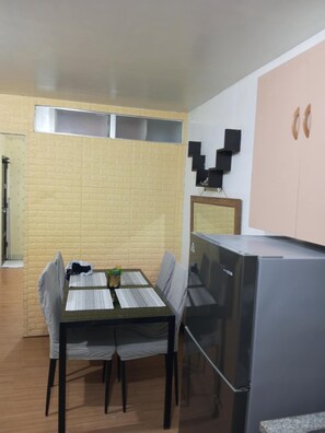 A compact kitchen with a dining table, chairs, a refrigerator, and a wall-mounted shelf. - Deca Homes - Hernan Cortes (Cebu City)