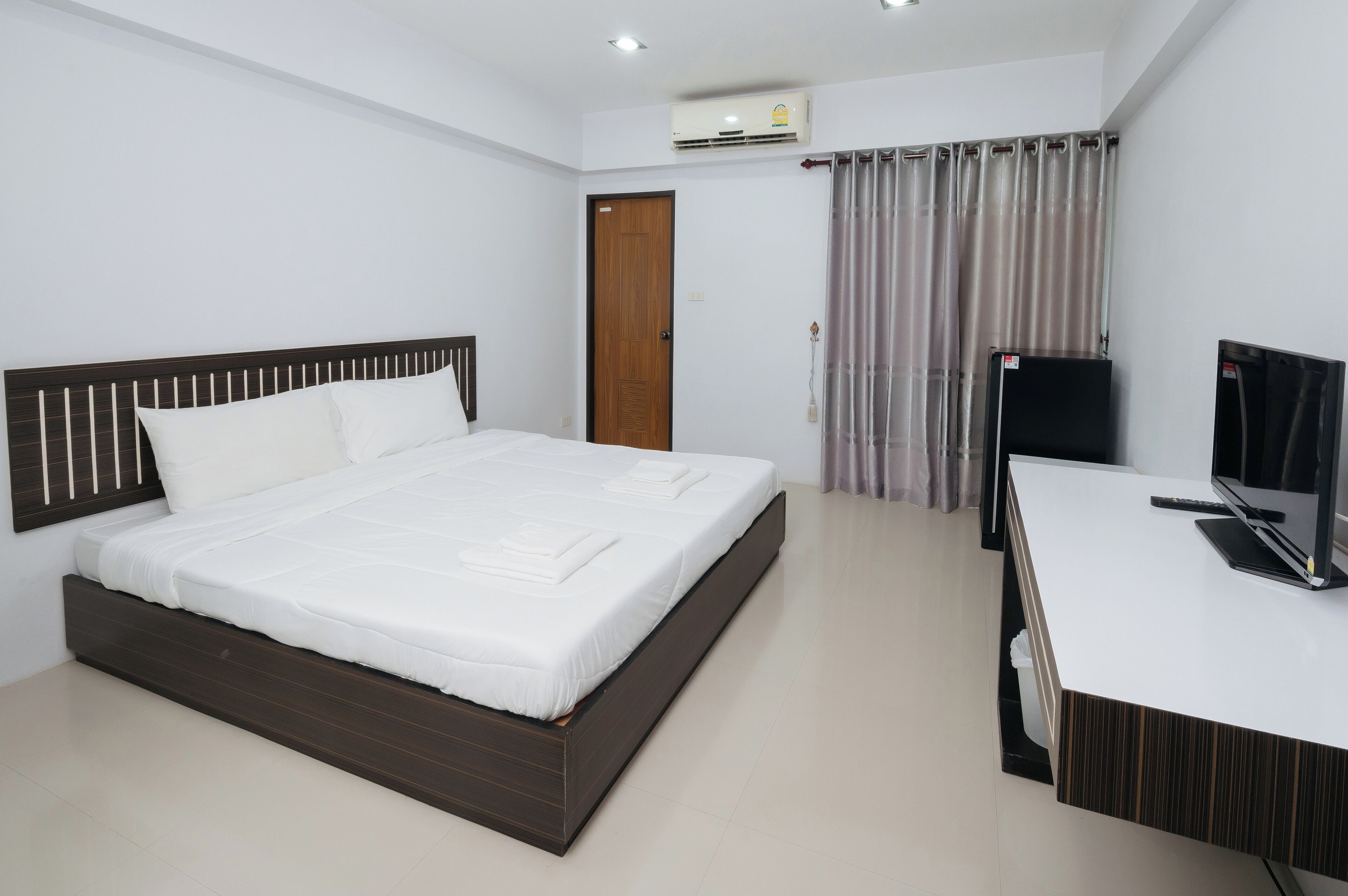 A bedroom with a bed, a desk, a television, an air conditioning unit, and a door.