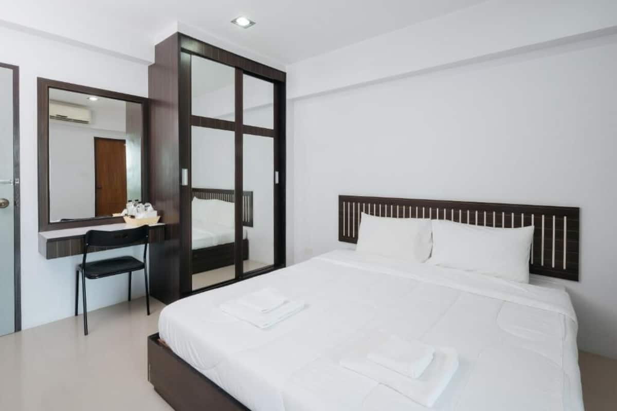 A modern hotel room with a large bed, a desk, a mirror, and a wardrobe.