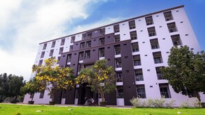 A multi-story building with a modern architectural design, featuring a combination of dark and light facade panels, and surrounded by a well-maintained grassy area with trees. - Creston Grand (Bang Pla Ma)