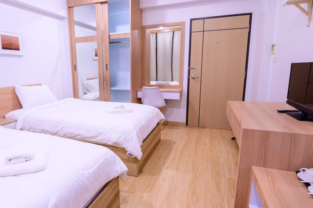 A hotel room with two beds, a wooden desk, a television, and a wardrobe.
