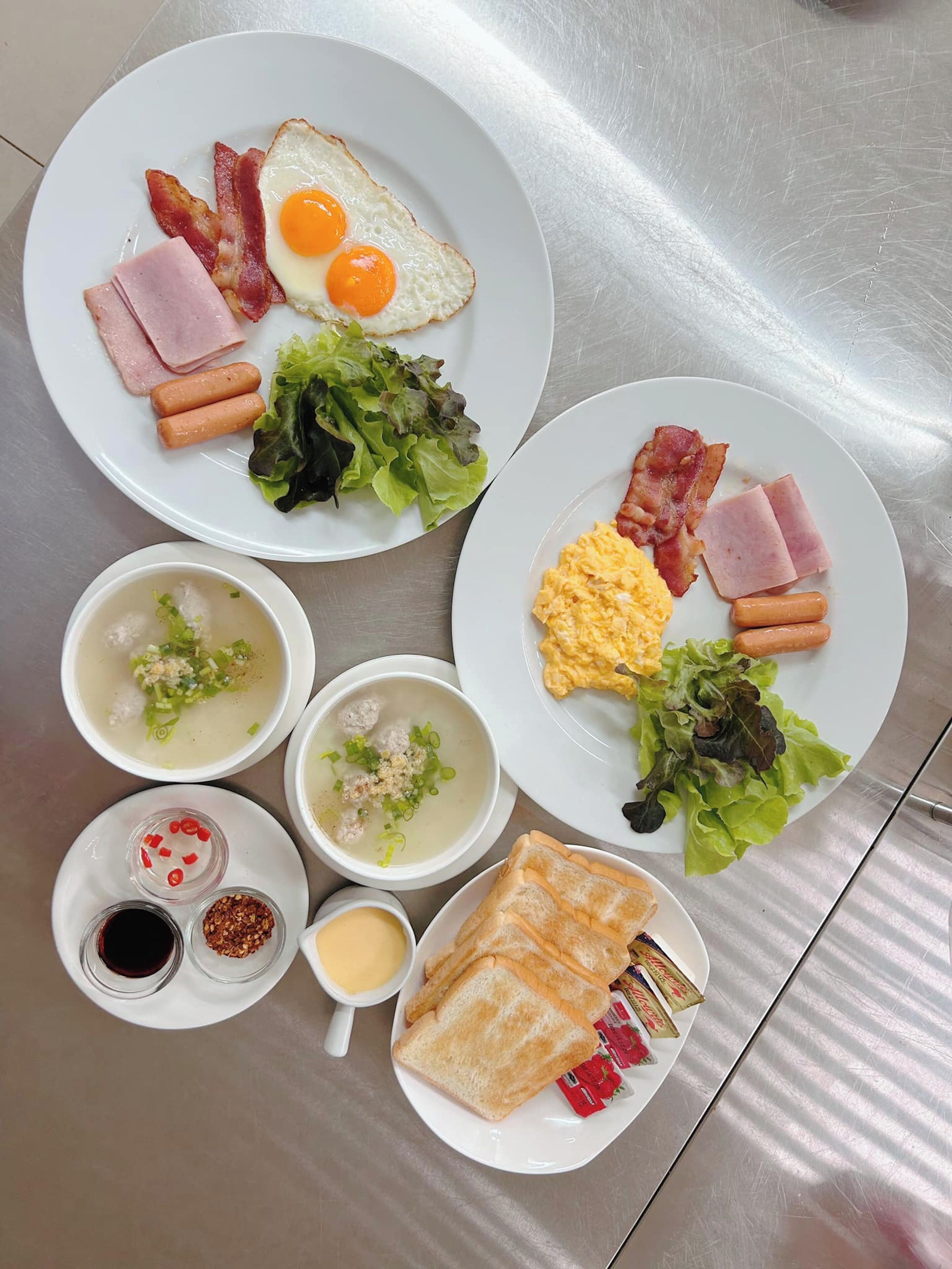 Une table mise pour le petit-déjeuner avec des assiettes contenant des œufs, du bacon, du jambon, des saucisses, des toasts et de la soupe.