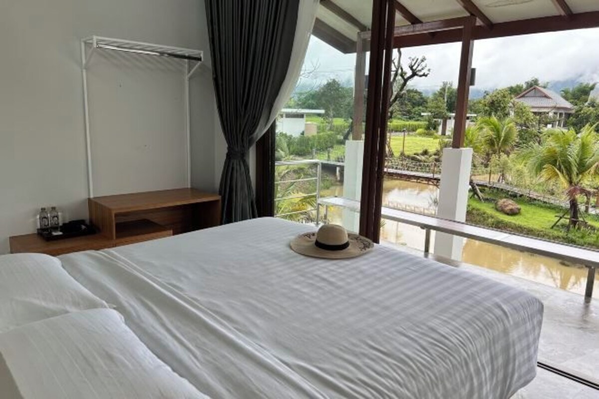 Une chambre à coucher avec un lit, une table de chevet, une fenêtre donnant sur un jardin et une maison.