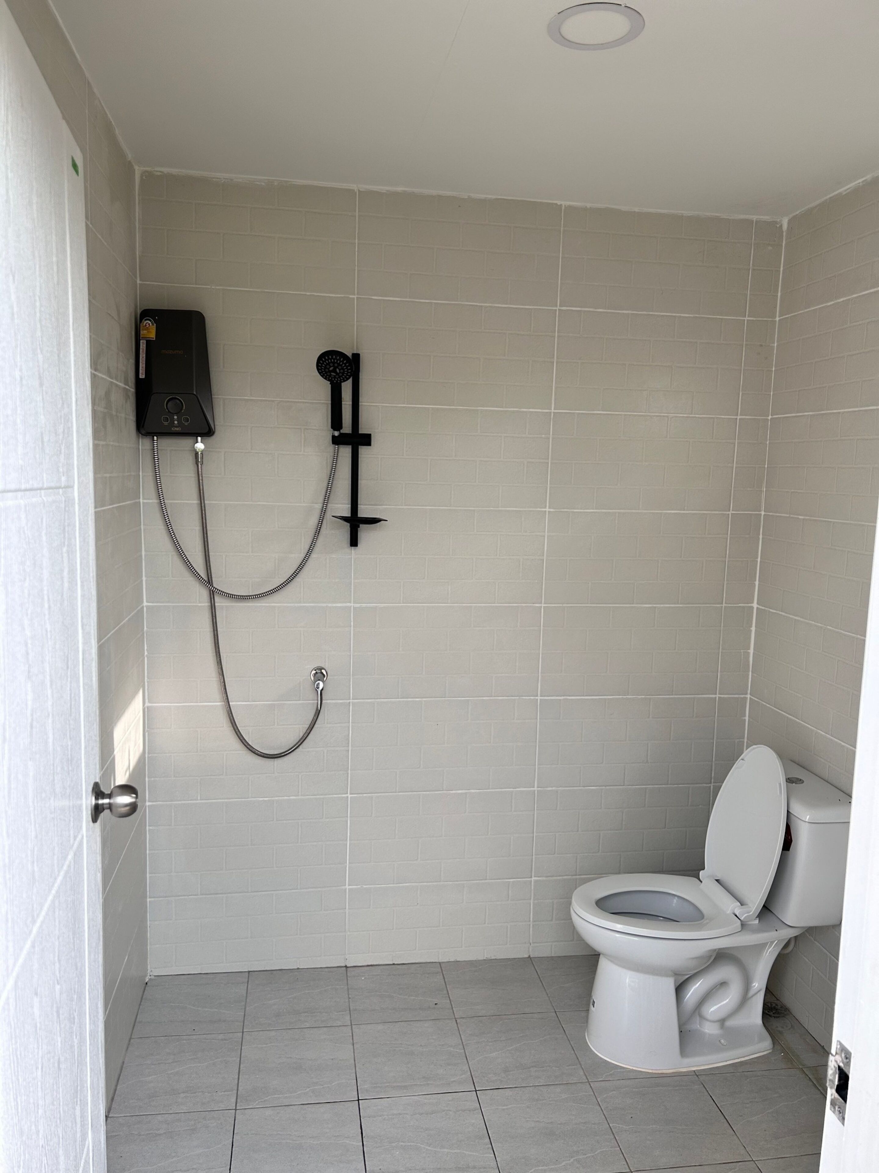 A bathroom with a toilet, a shower unit, and tiled walls.
