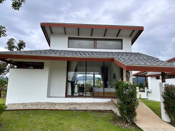 Uma casa moderna de dois andares com telhado plano, janelas amplas e um espaço de varanda coberto.