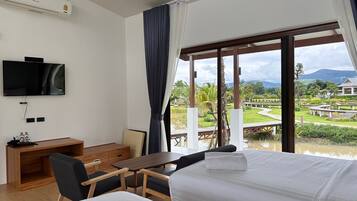 A hotel room with a bed, a desk, a chair, a TV, and a large window with a view of a golf course and mountains.