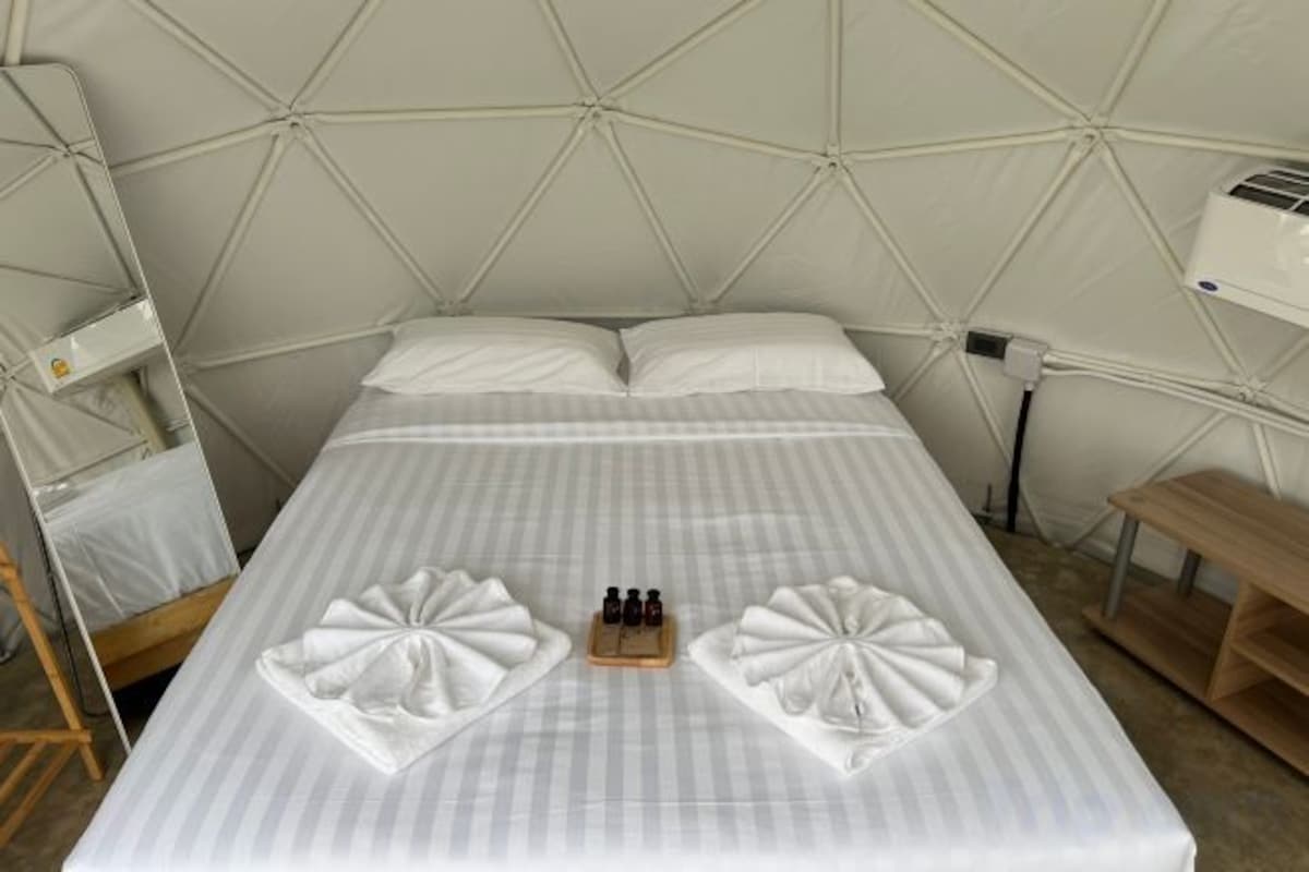 Un lit avec une couvre-lit à rayures, deux serviettes pliées posées sur le lit et une table de chevet avec une bouteille.