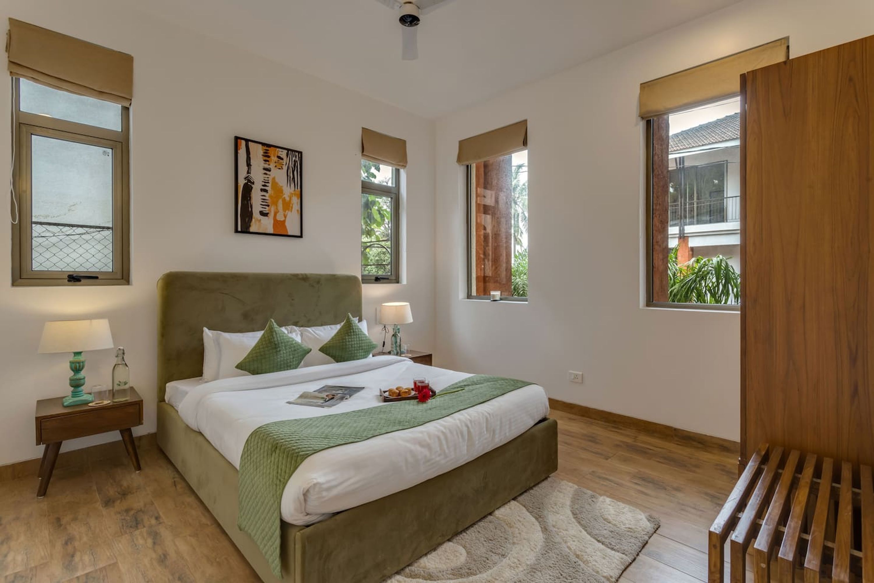 A neatly arranged bedroom with a large bed, two bedside tables, and a view of the outside through windows.