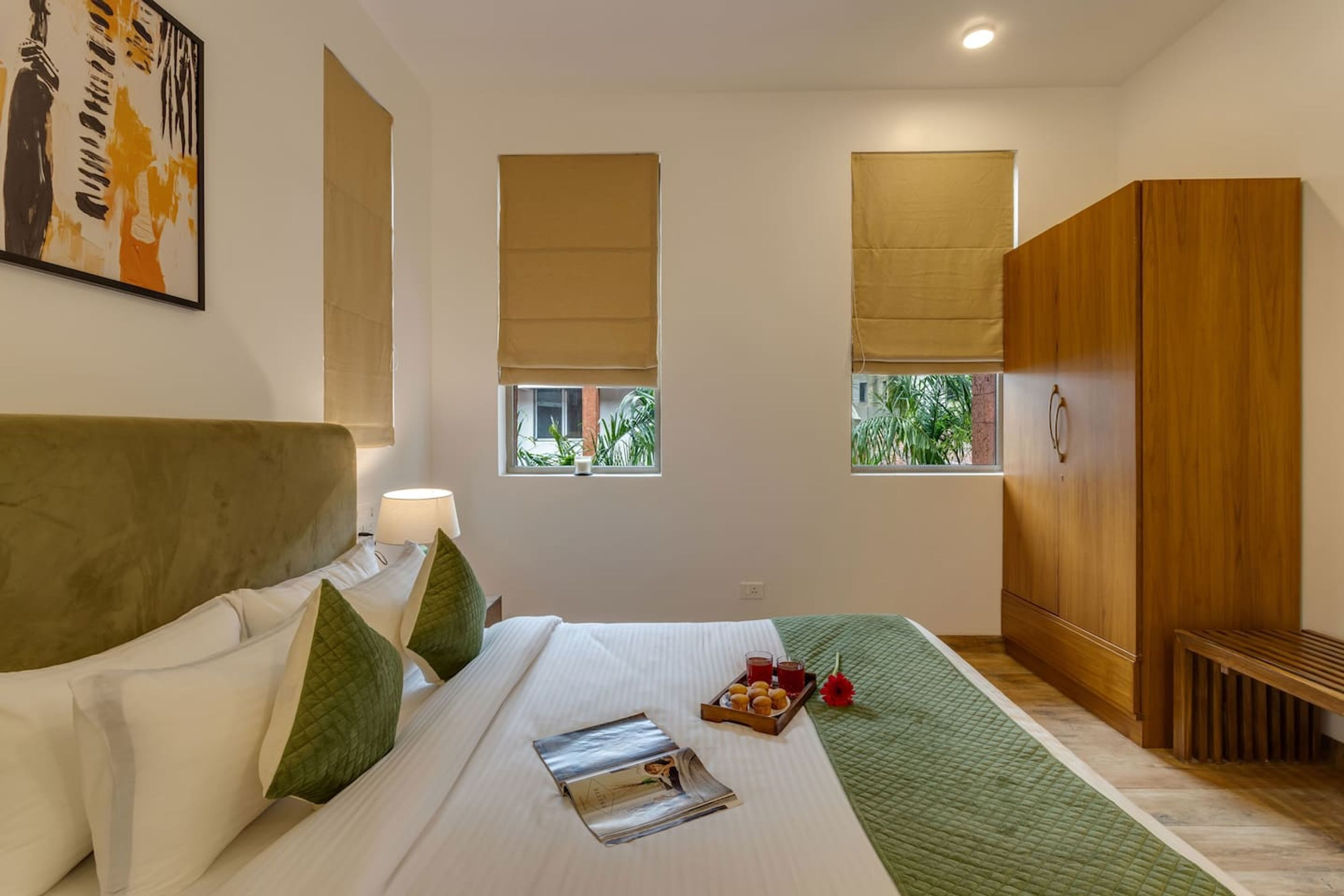 Ein Hotelzimmer mit Bett, Nachttisch, Lampe, Fenster mit Blick auf Grünflächen und einem Holzschrank.