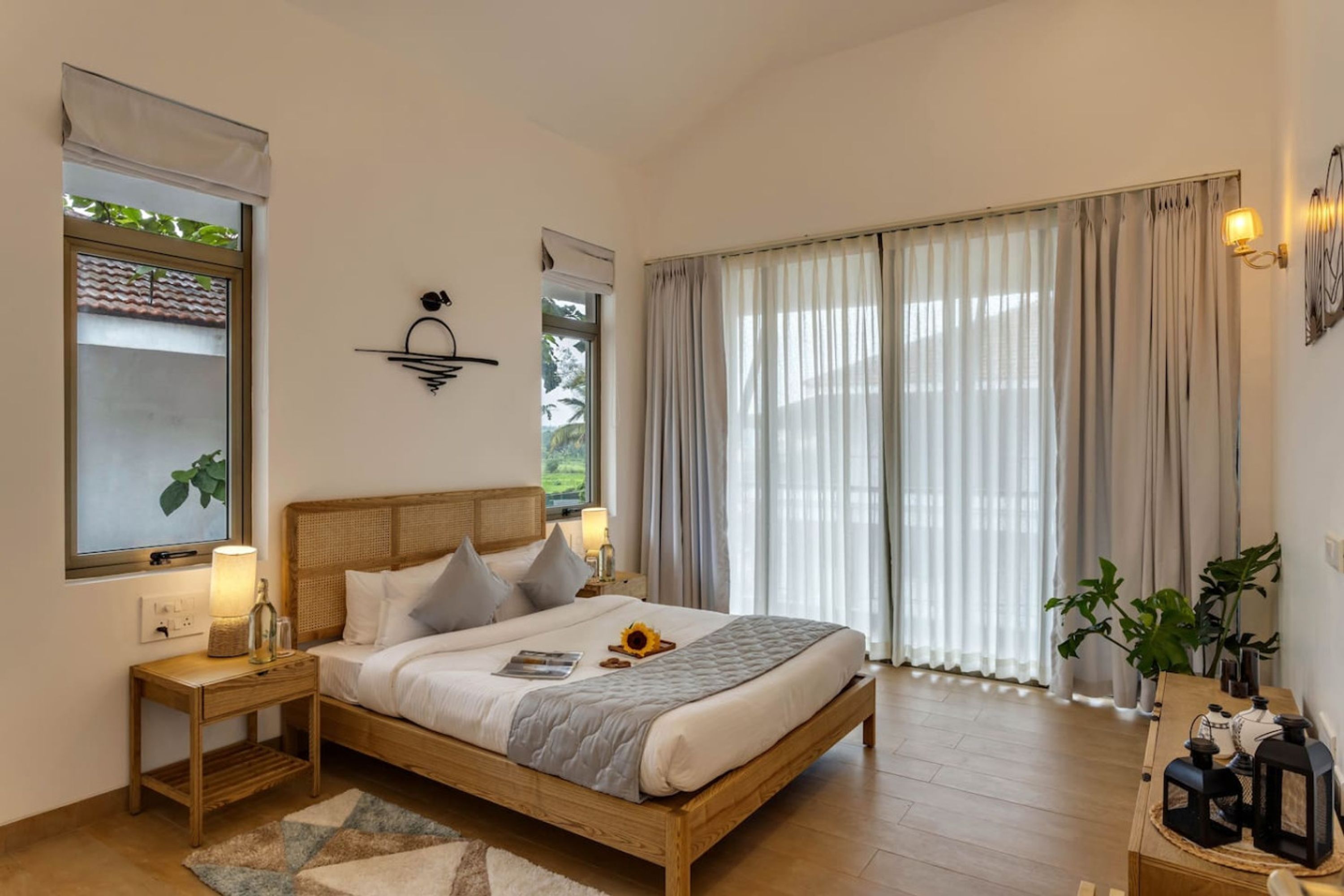 A bedroom with a wooden bed, bedside tables, a nightstand, a window with curtains, and a wall-mounted light fixture.