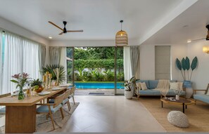 A modern living room with a dining area, a pool, and a view of lush greenery. - Casa Maxima - 4BR w Private Pool 1km to the Beach (Nerul)